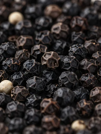 Guľôčky čierneho korenia a mleté korenie v keramickej miske na drevenom povrchu