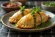Zlatisté upečené empanadas na drevenej doske s miskou zelenej omáčky