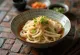 Kishimen udon v miske, ploché udon rezance v bohatom vývare dashi, zdobené čerstvou zelenou cibuľkou a sezamom